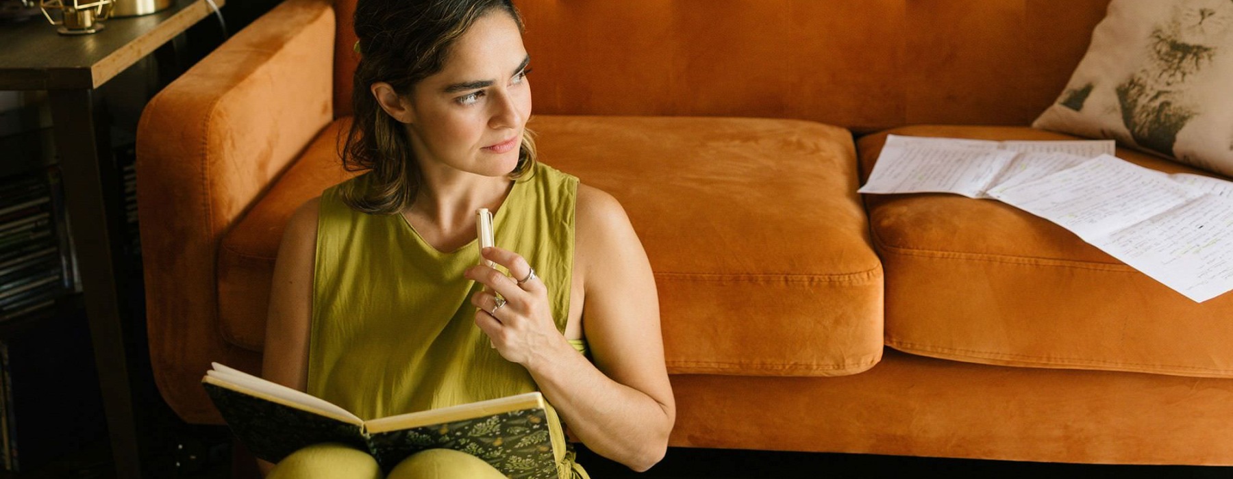 A woman sitting in front of a couch writing in a journal